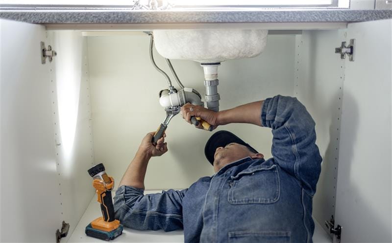 Plumber repairing pipes beneath a bathroom sink in Bartow