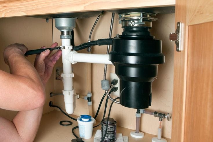 Plumber installing a garbage disposal beneath a kitchen sink in Bartow