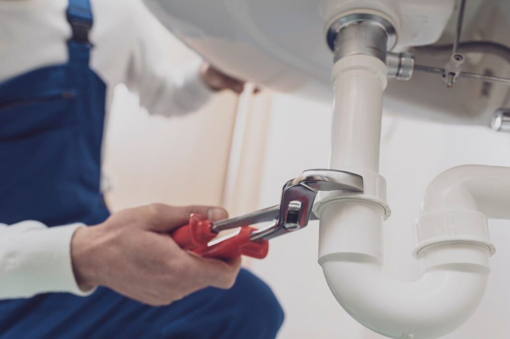 Plumber repairing a white drain pipe beneath a sink in Bartow