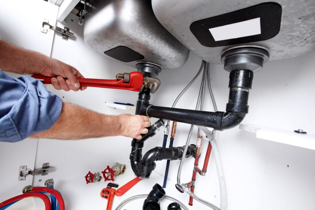 Plumber repairing drain pipes beneath a kitchen sink in Bartow